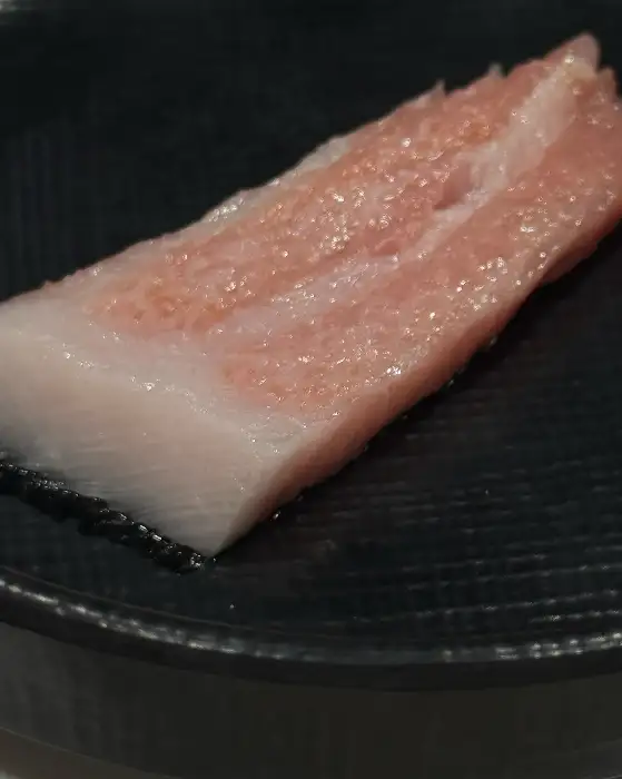 한 점의 두툼한 참치회가 검은 접시에 담겨 있는 모습. 섬세한 지방층이 빛나고 있다.