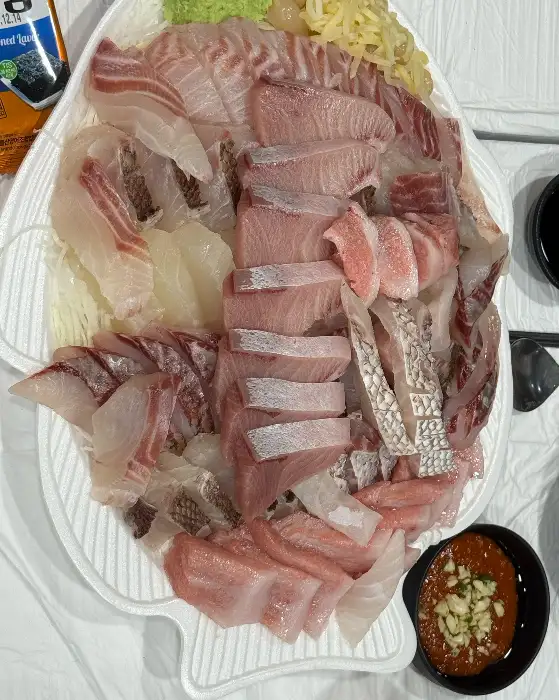 물고기 모양의 접시에 여러 종류의 회가 푸짐하게 담겨 있는 모습. 옆에는 쌈 채소와 소스가 준비되어 있다.