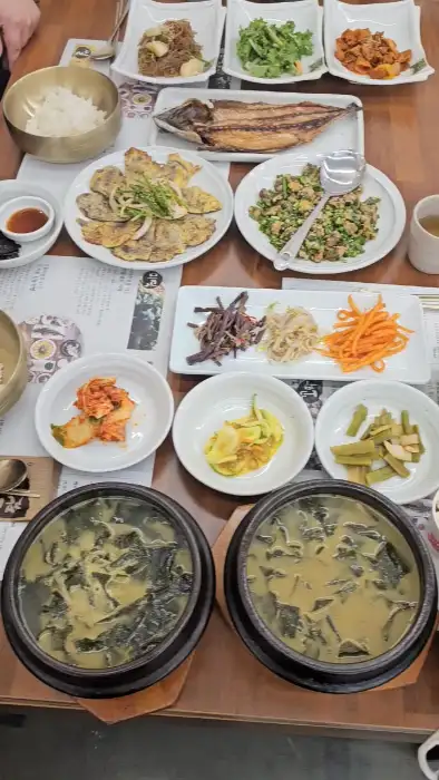 두 개의 뚝배기에 담긴 미역국과 여러 가지 반찬이 올라간 식탁