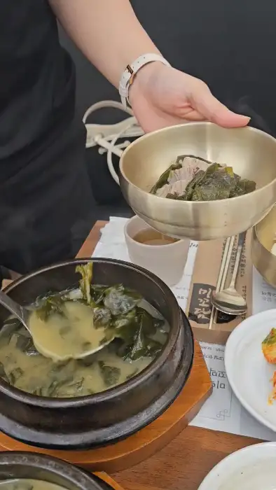 한 손으로 놋그릇에 담긴 미역국을 덜어내는 모습
