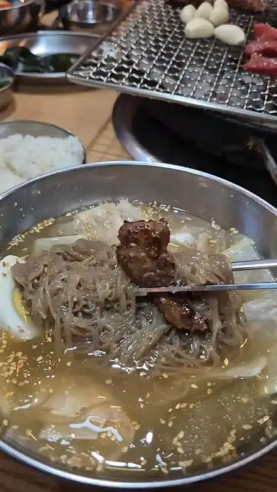 시원한 국물의 냉면에 고기 한 점을 얹은 모습